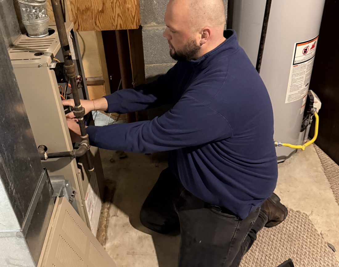 A Commodore Heating & Cooling technician servicing a furnace and water heater in a Toledo-area home